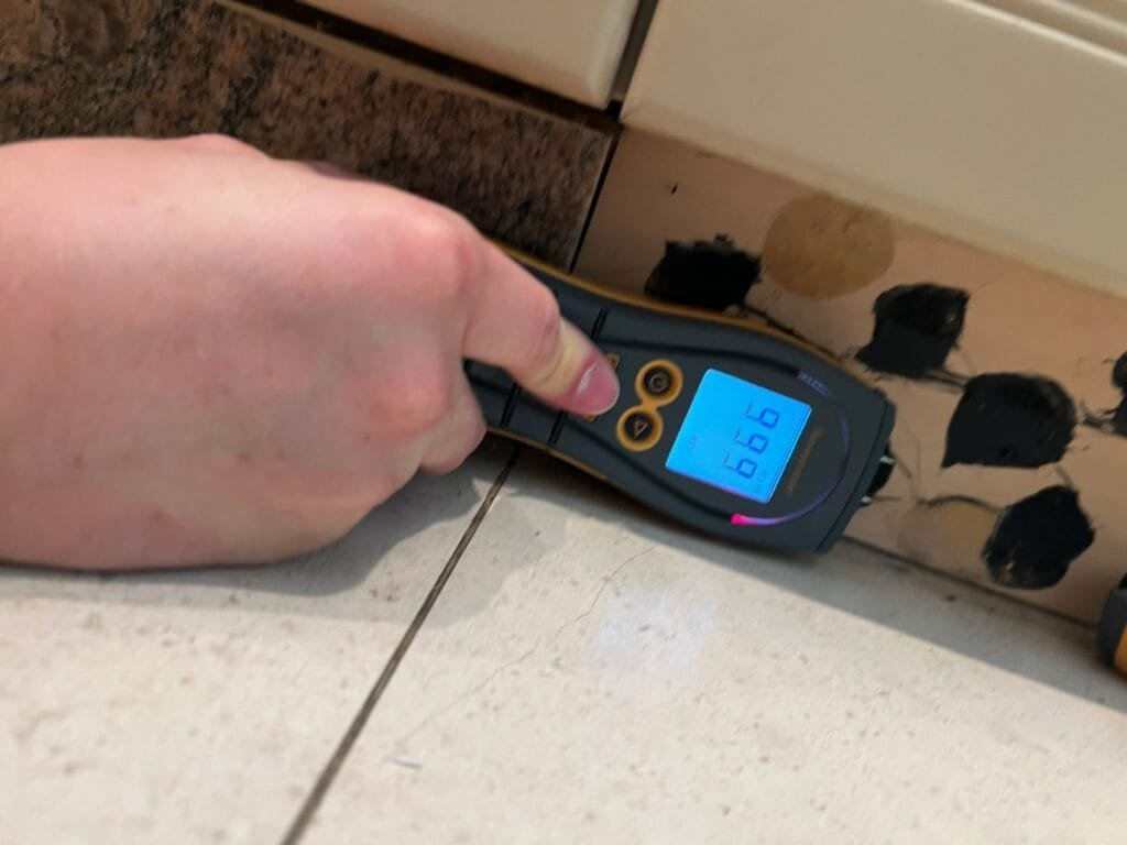 Moisture meter at a kitchen cabinet base with mold at the toe-kick after a dishwasher leak in Calabasas