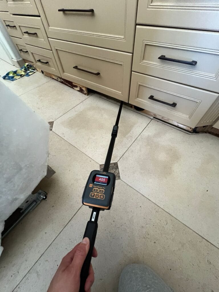 Long-reach moisture probe measuring water under stained stone tile in a Calabasas kitchen