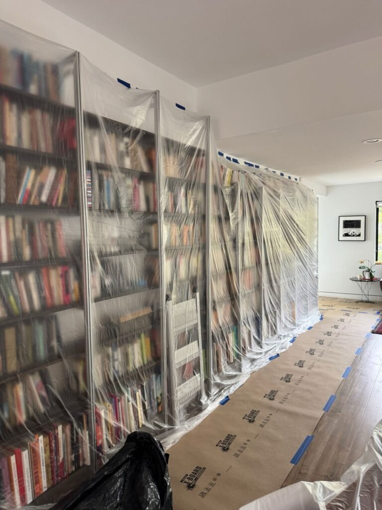 Wall of bookshelves wrapped in plastic and floors covered before restoration work in a Hollywood Hills home