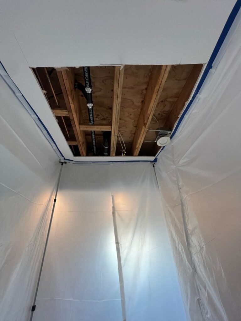 Ceiling opened inside containment, showing the drain pipes, after a toilet leak in a Hollywood Hills home