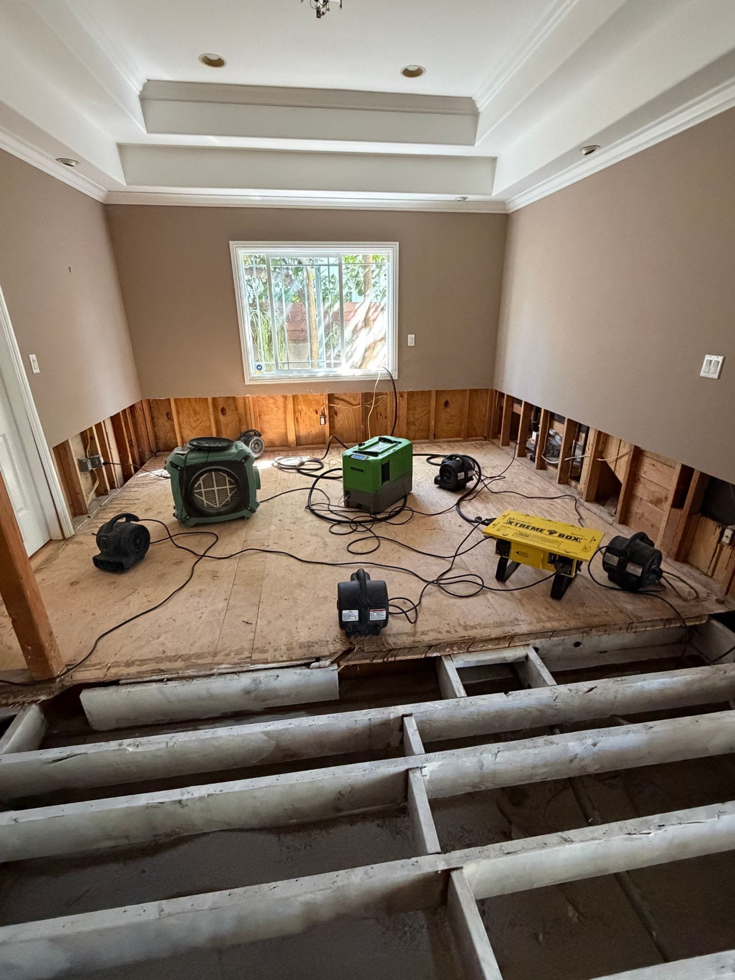 Air movers and a dehumidifier drying a bedroom after flood cuts and flooring removal