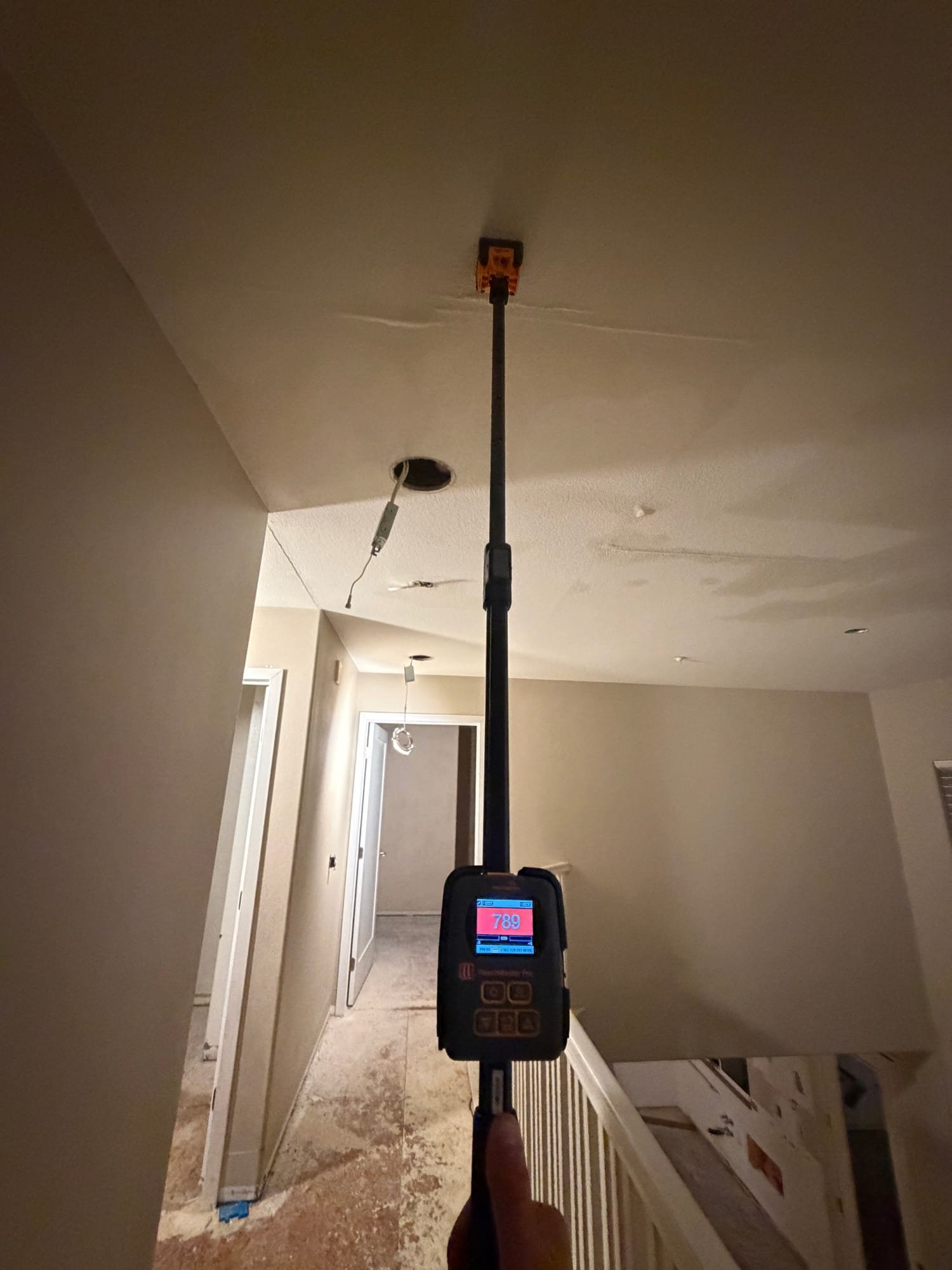 Moisture meter on an extension pole checking a water-stained ceiling during a water damage inspection